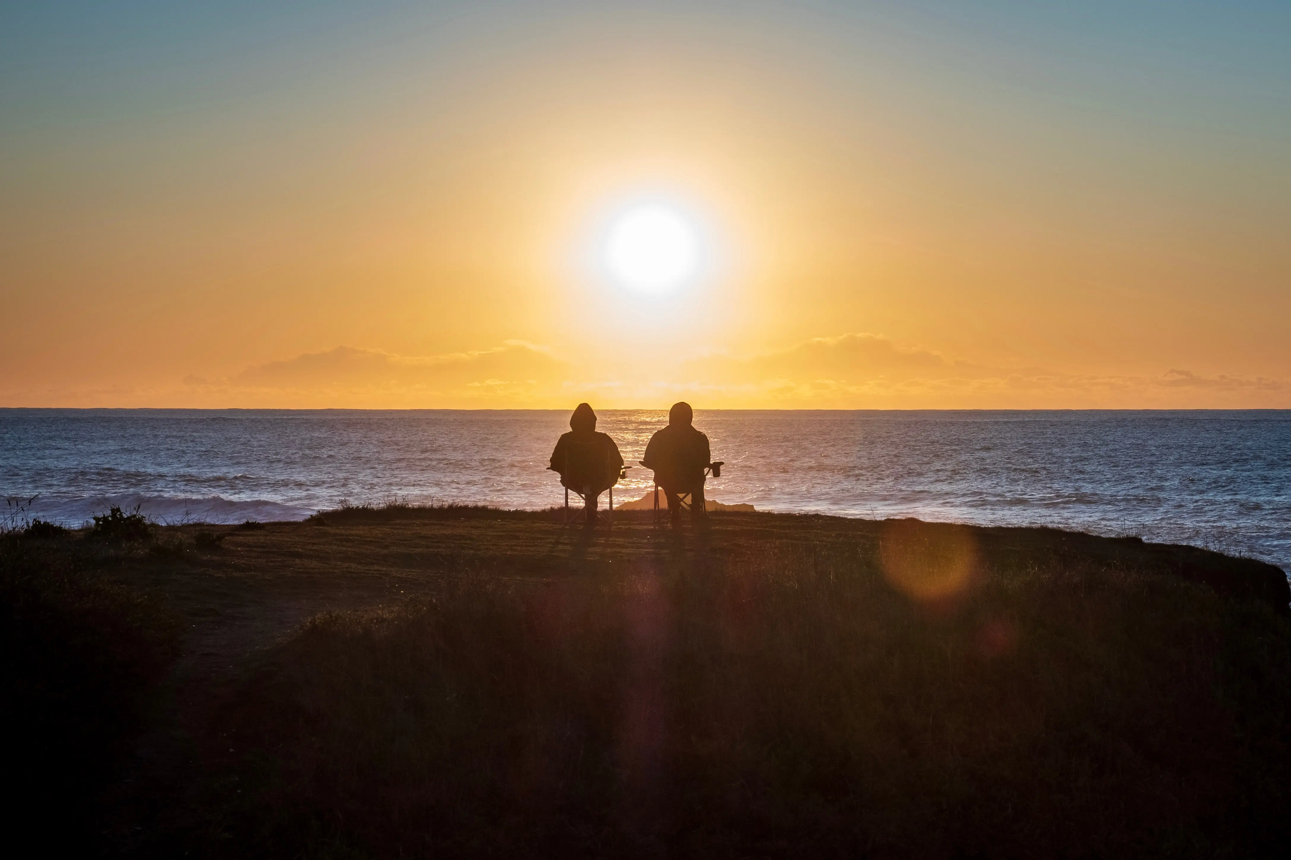 Deux personnes assises au bord d'une falaise, coucher de soleil