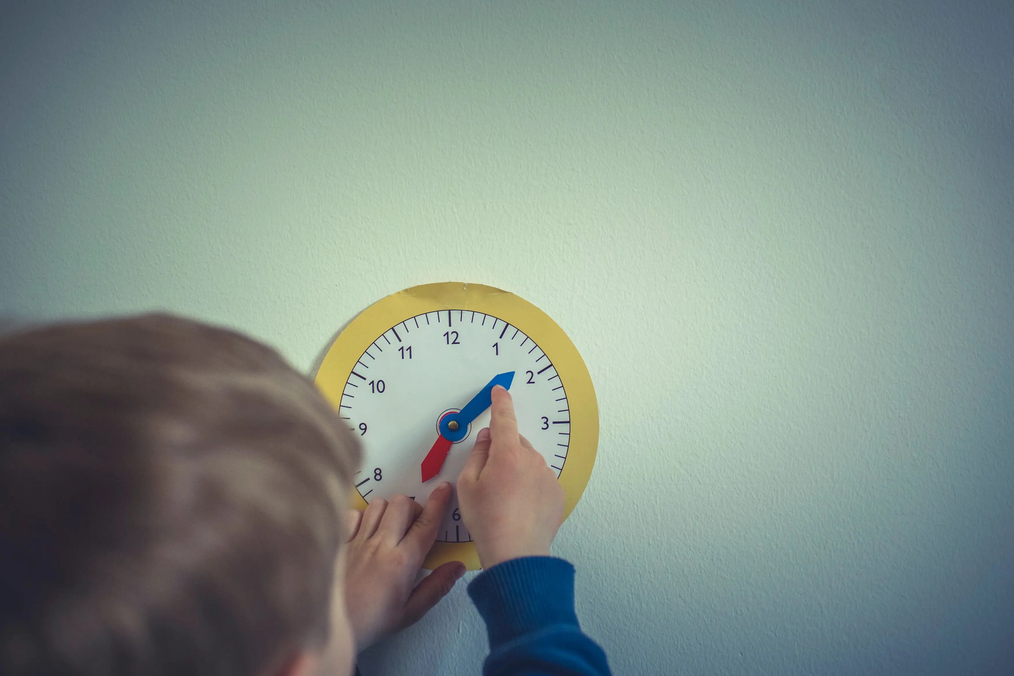 Garçon tournant les aiguilles d'une horloge en papier, accrochée sur un mur blanc