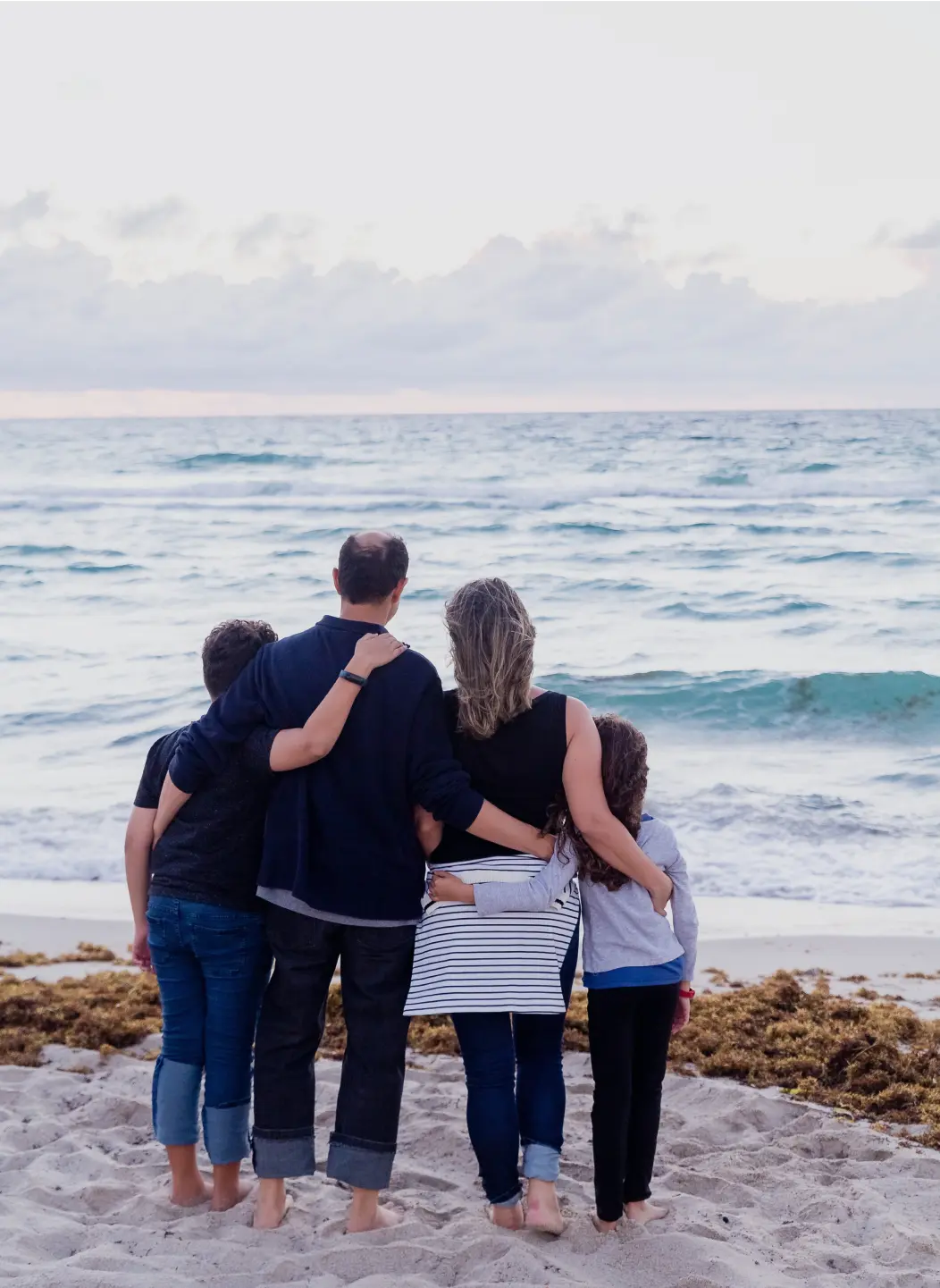 Famille sur une plage regardant la mer en se tenant dans les bras.
