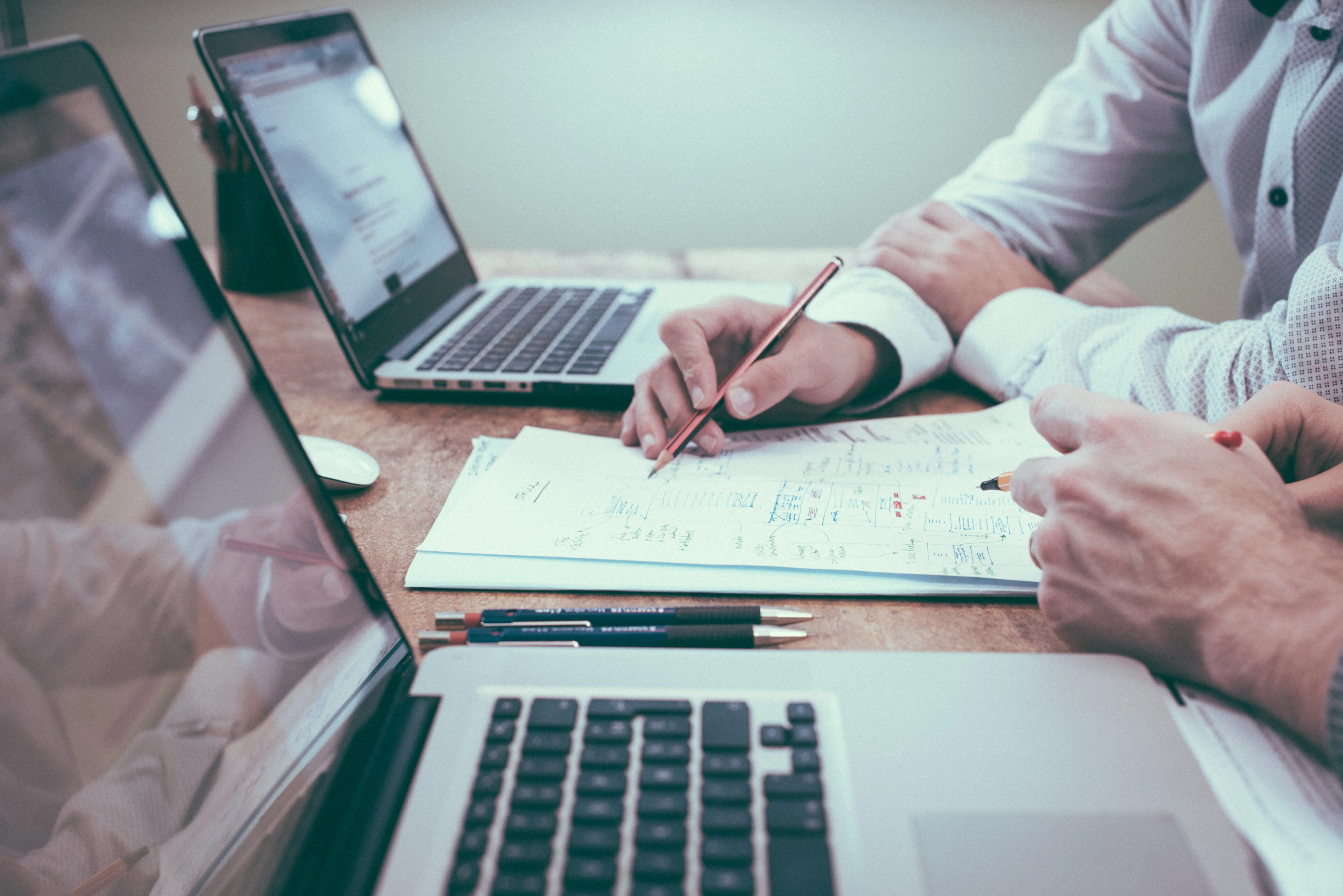 Deux hommes discutent sur un bureau, ordinateurs, feuilles