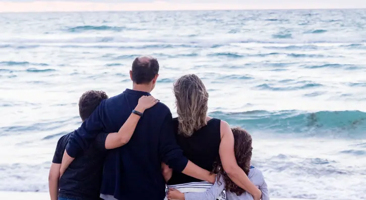 Famille sur une plage regardant la mer en se tenant dans les bras.