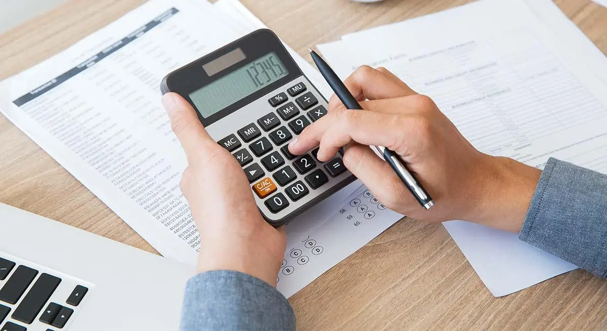 Homme tenant une calculatrice, feuilles d'imposition, bureau en bois